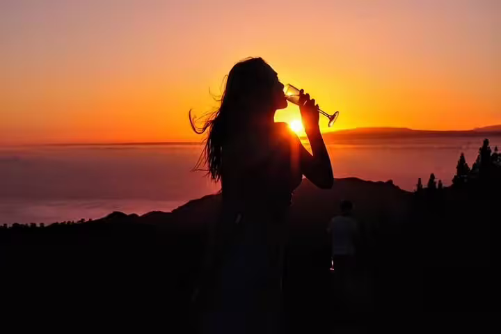 Woman sipping wine while watching a stunning sunset on Mount Teide, enhancing the stargazing and dining tour ambiance.