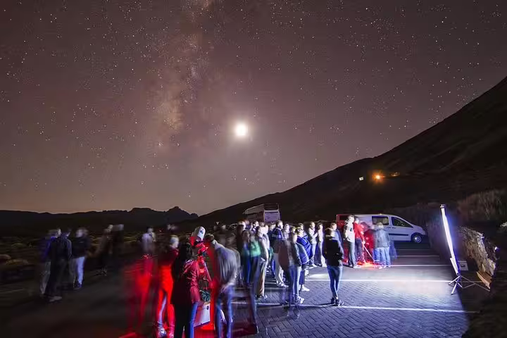 Tourists stargazing at Mount Teide under a clear sky filled with stars and a bright moon, perfect for night tours.