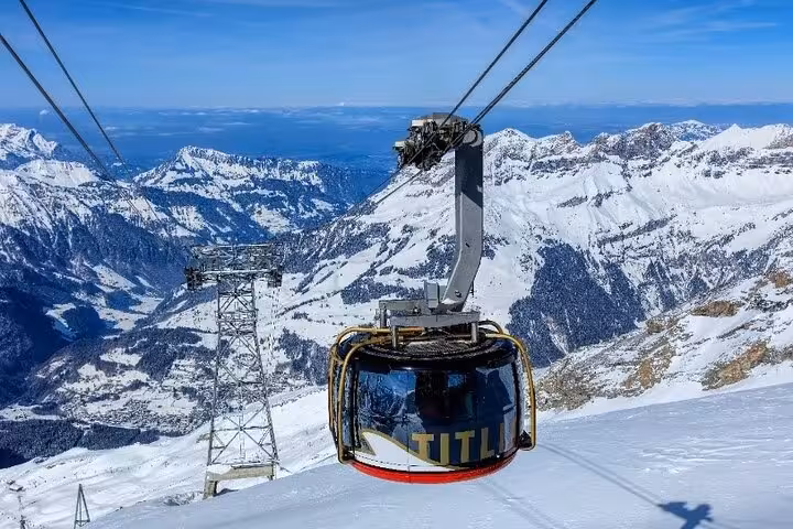 Snow-covered peaks surround a cable car ascending Mount Titlis, offering breathtaking alpine views on a private tour.