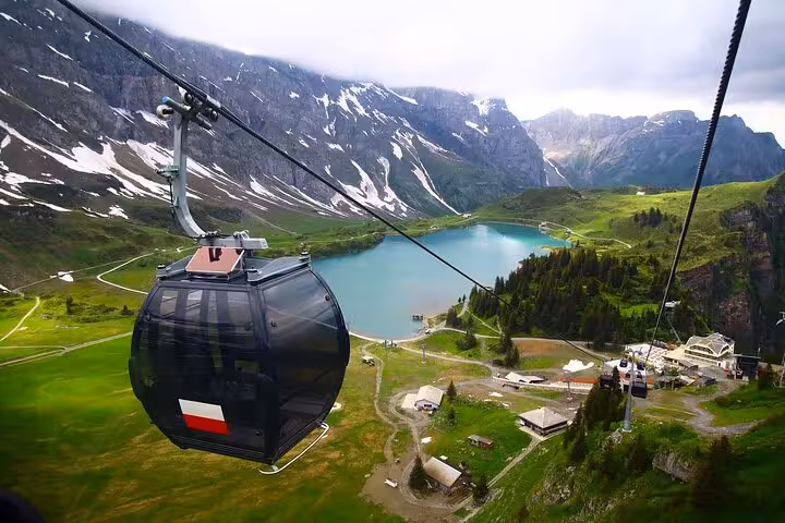 Scenic cable car ride over lush green valleys and a picturesque lake heading to Mount Titlis on a private tour.
