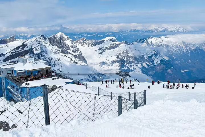 Tourists enjoy a snowy day at Mount Titlis with stunning views of the Swiss Alps, perfect for a winter adventure.