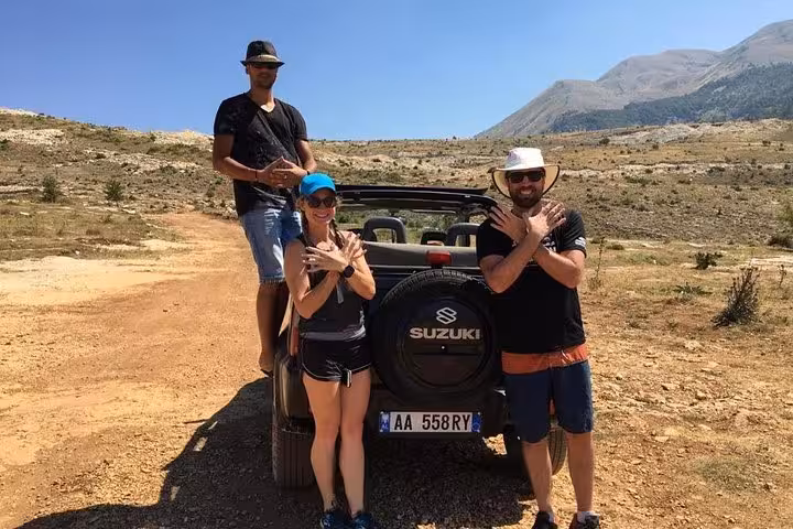 Adventurers posing with a 4x4 Suzuki on a rugged trail near Mount Tomorr during a guided off-road tour.