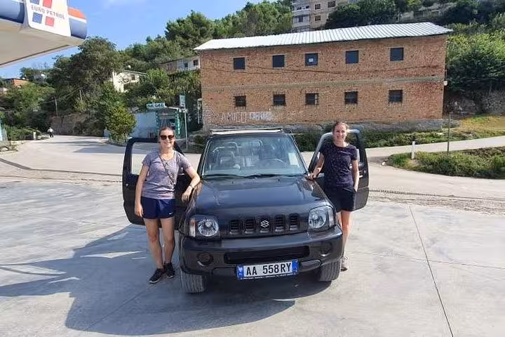 Two travelers standing beside a parked 4x4 vehicle, ready for a hiking adventure near Bogove Waterfall.