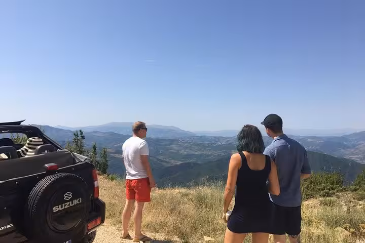 Three travelers admire panoramic mountain views next to a 4x4 vehicle on a guided tour to Mount Tomorr.