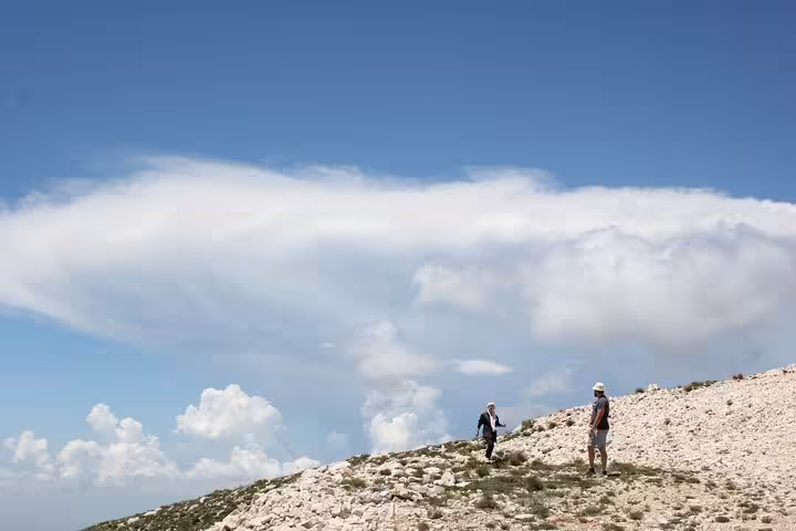 Hikers traverse rocky terrain on Mount Tomorr with dramatic cloud formations, highlighting a thrilling hiking experience.