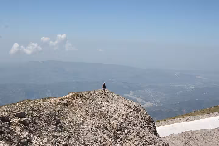 Hiker stands on rocky Mount Tomorr summit with expansive valley views, perfect for 4x4 adventures and hiking tours.