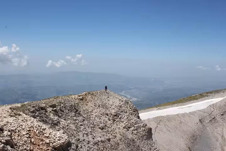 A lone figure stands on the rocky summit of Mount Tomorr, offering breathtaking panoramic views ideal for hiking tours.