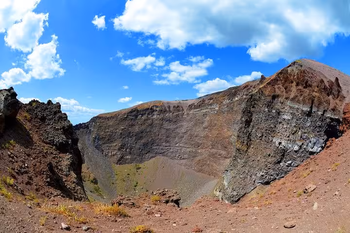 Crater of Mount Vesuvius under a bright blue sky, showcasing its rugged volcanic terrain and historical significance.