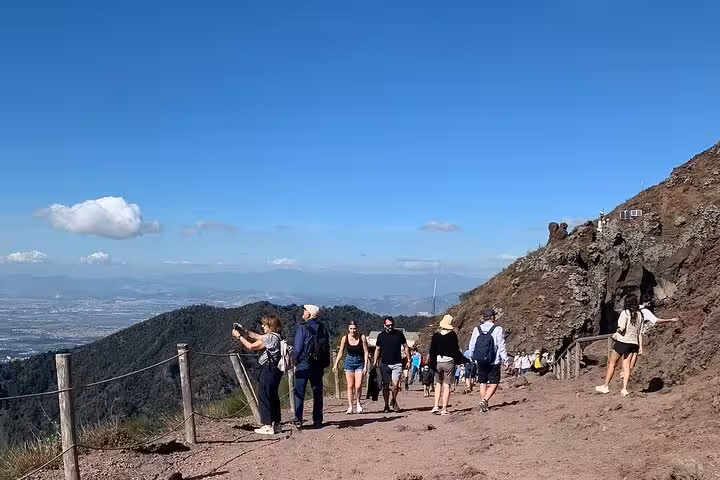 Tourists enjoying a guided walk along the scenic trails of Mount Vesuvius under a clear blue sky.