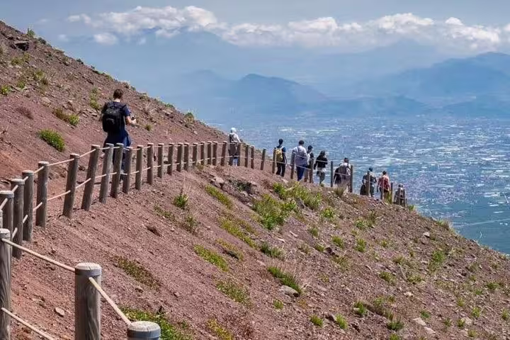 Tourists walking along a scenic trail on Mount Vesuvius with panoramic views, part of a guided tour from Sorrento.