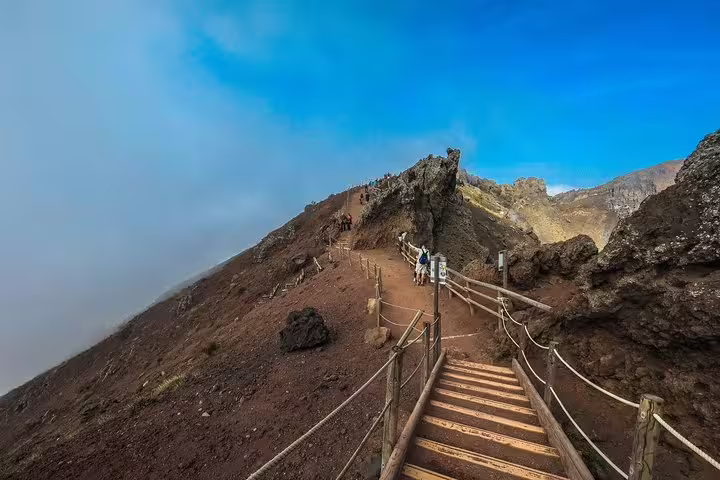 Visitors ascending a wooden path on Mount Vesuvius under a clear blue sky, enjoying a guided tour experience.