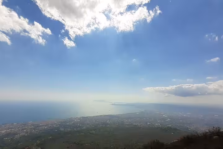 Expansive panorama from Mount Vesuvius showcasing the Gulf of Naples with sunlit clouds and serene sea views.