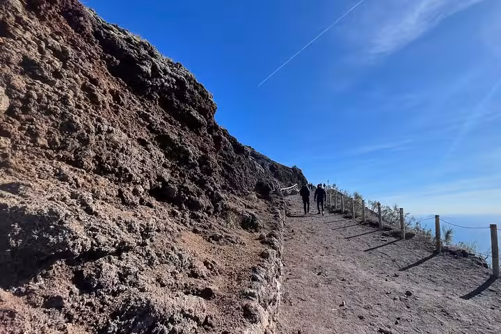 Tourists hike a rocky path on Mount Vesuvius under a clear blue sky during a small group tour from Sorrento.