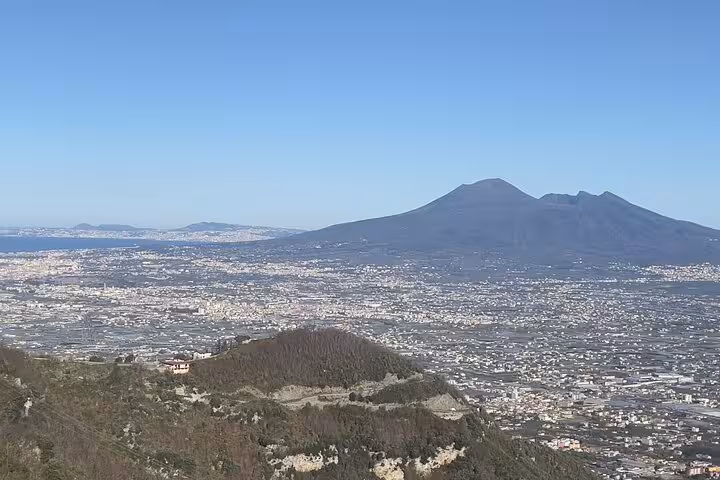 Expansive view of Mount Vesuvius towering over the cityscape and coastline under a bright blue sky.