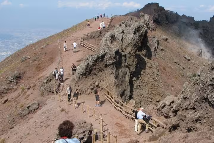 Tourists walk along the scenic trails of Mount Vesuvius, capturing the rugged beauty of this iconic Sorrento day trip.