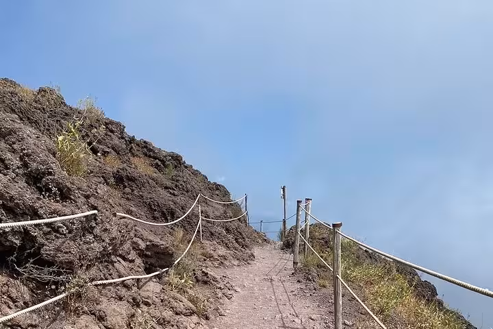 A rugged path leading to the summit of Mount Vesuvius, bordered by ropes and rocky terrain.