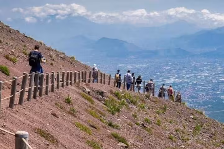 Visitors walking along the rugged path of Mount Vesuvius with stunning views of the surrounding landscape.
