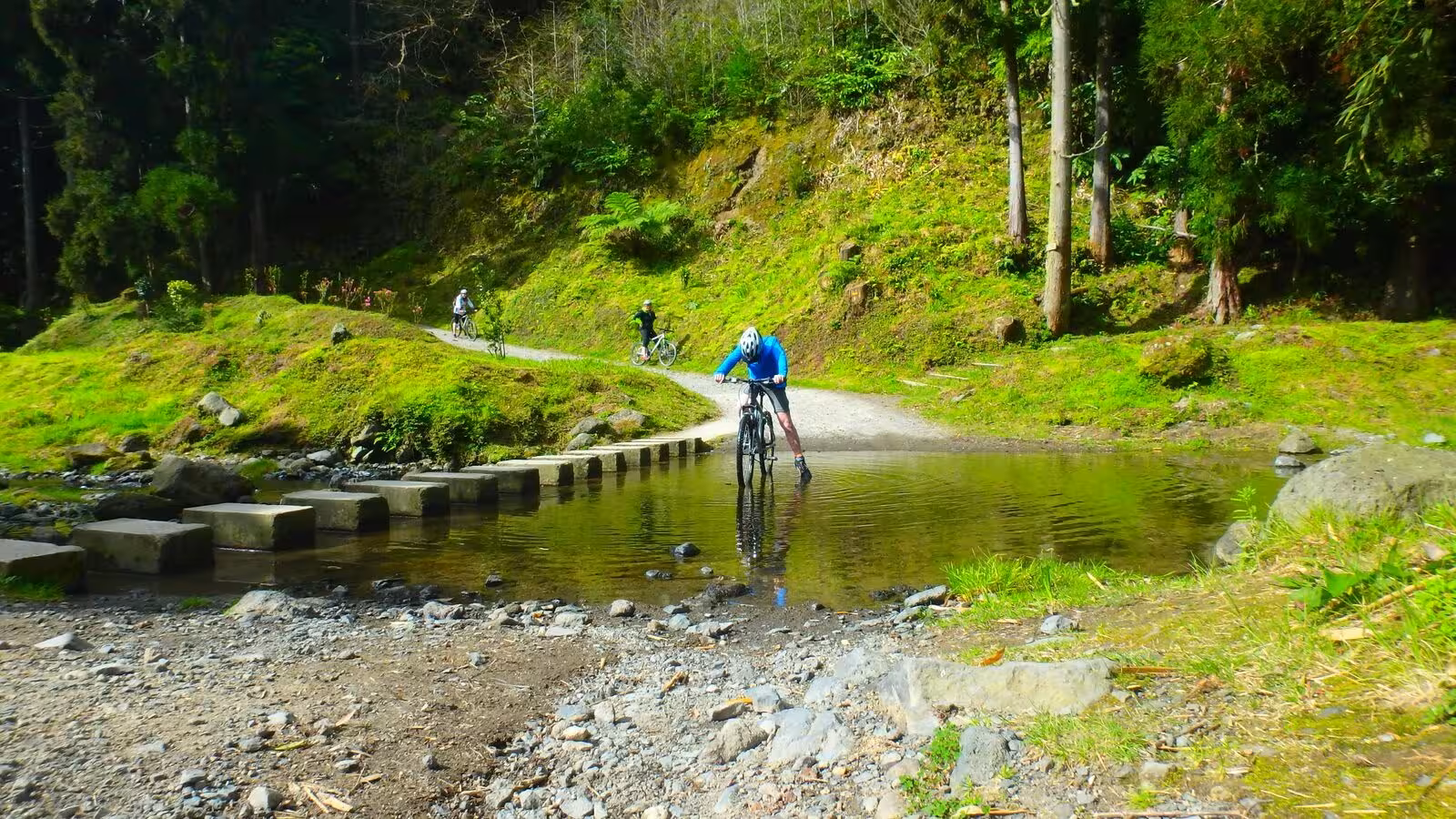 Mountain biker crossing a shallow stream on Furnas half-day bike tour trails in São Miguel, Azores