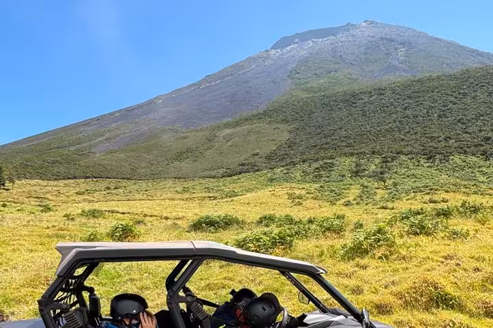 Buggy riders traverse vibrant green meadows at the base of a majestic mountain on an adventure-filled tour.