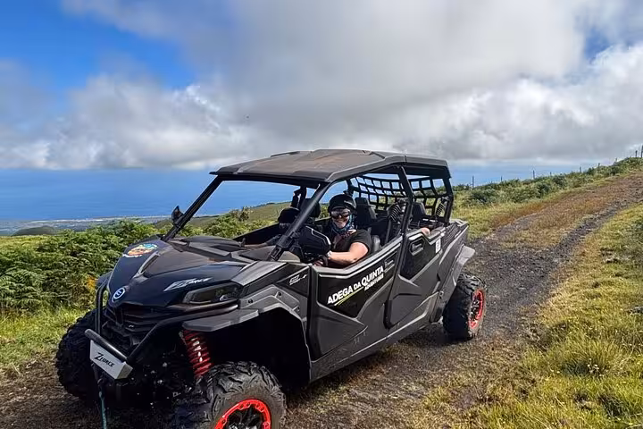 Adventurers enjoy a thrilling buggy ride on a scenic mountain trail overlooking the ocean under a clear blue sky.