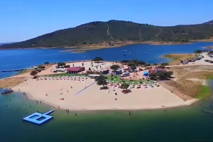 Aerial view of Moura's beach area by Alqueva Lake, featuring sun umbrellas and clear waters for a perfect day trip.