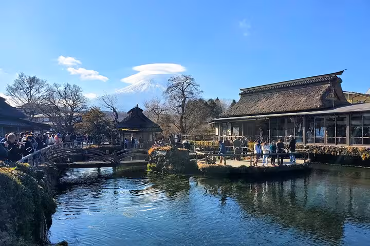 Visitors enjoying the scenic view of Mt. Fuji from a picturesque pond in a traditional Japanese setting.