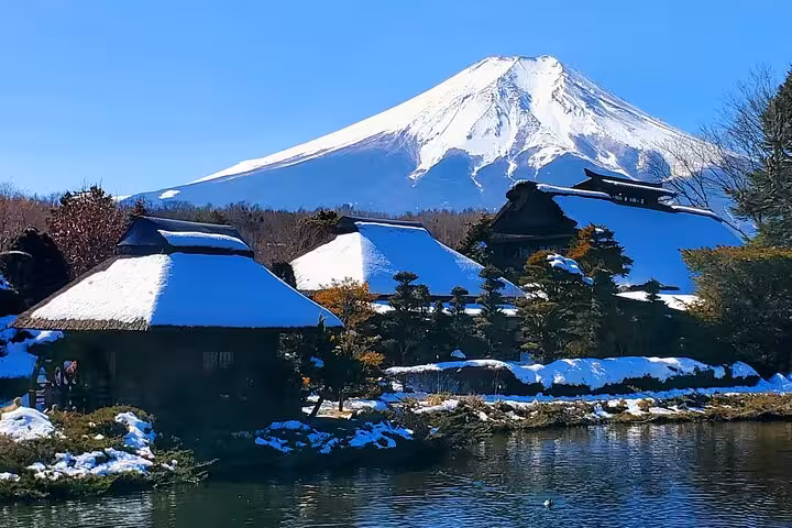 Scenic view of Mt. Fuji with traditional thatched-roof houses and a tranquil pond in Hakone, Japan.