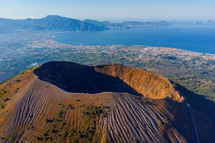 Aerial view of Mt. Vesuvius crater and the stunning Bay of Naples, showcasing the volcanic landscape.