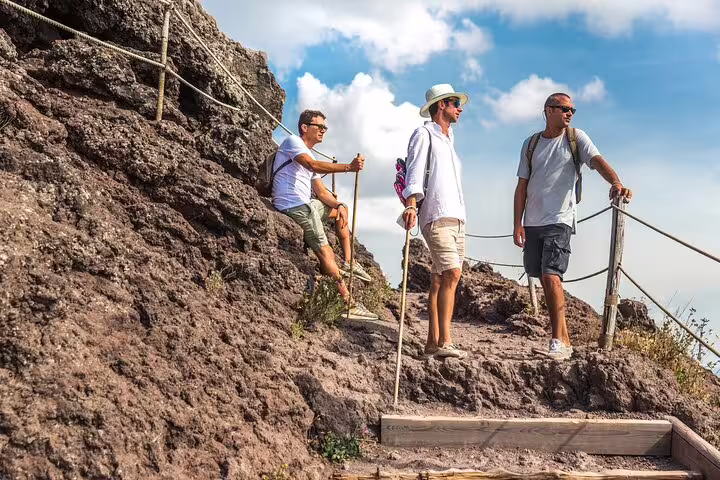 Hikers pause on rocky terrain of Mt. Vesuvius, capturing scenic vistas during a guided tour from Sorrento.