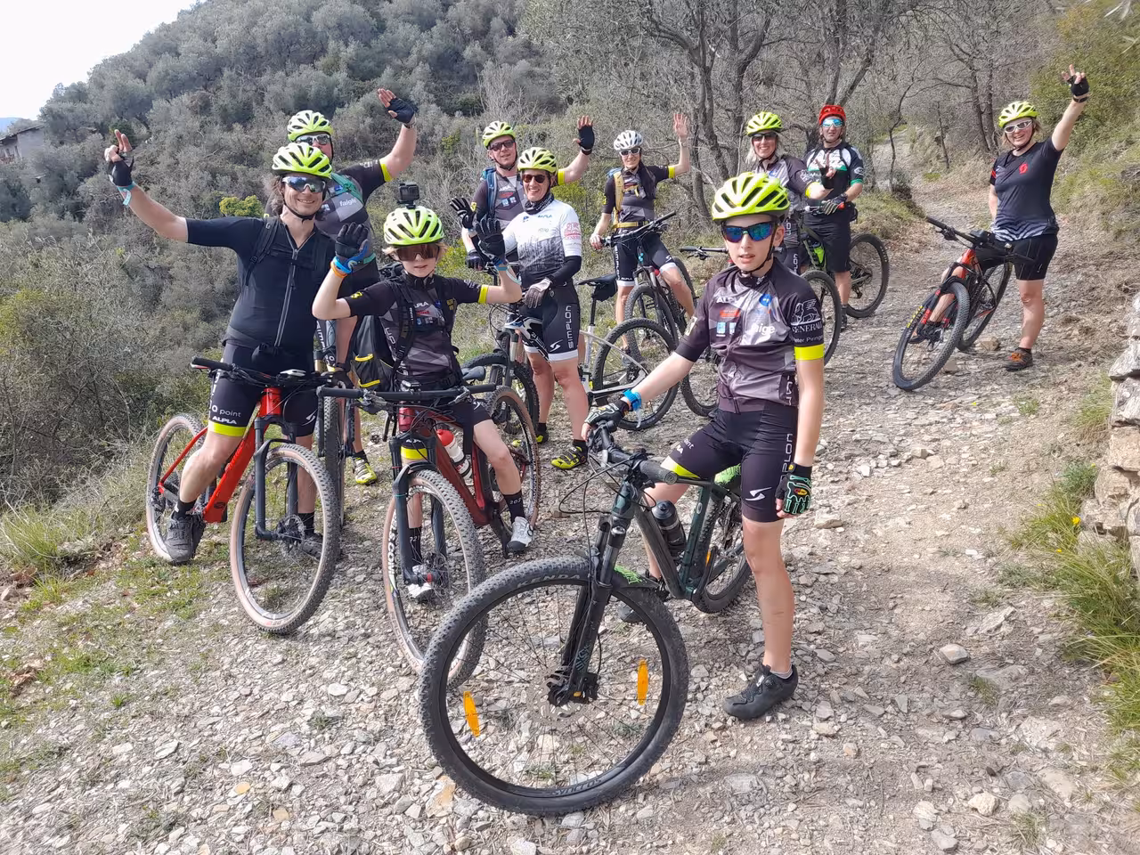 Gruppo misto di adulti e ragazzi in mountain bike durante un corso base di MTB su sentiero sterrato panoramico in collina