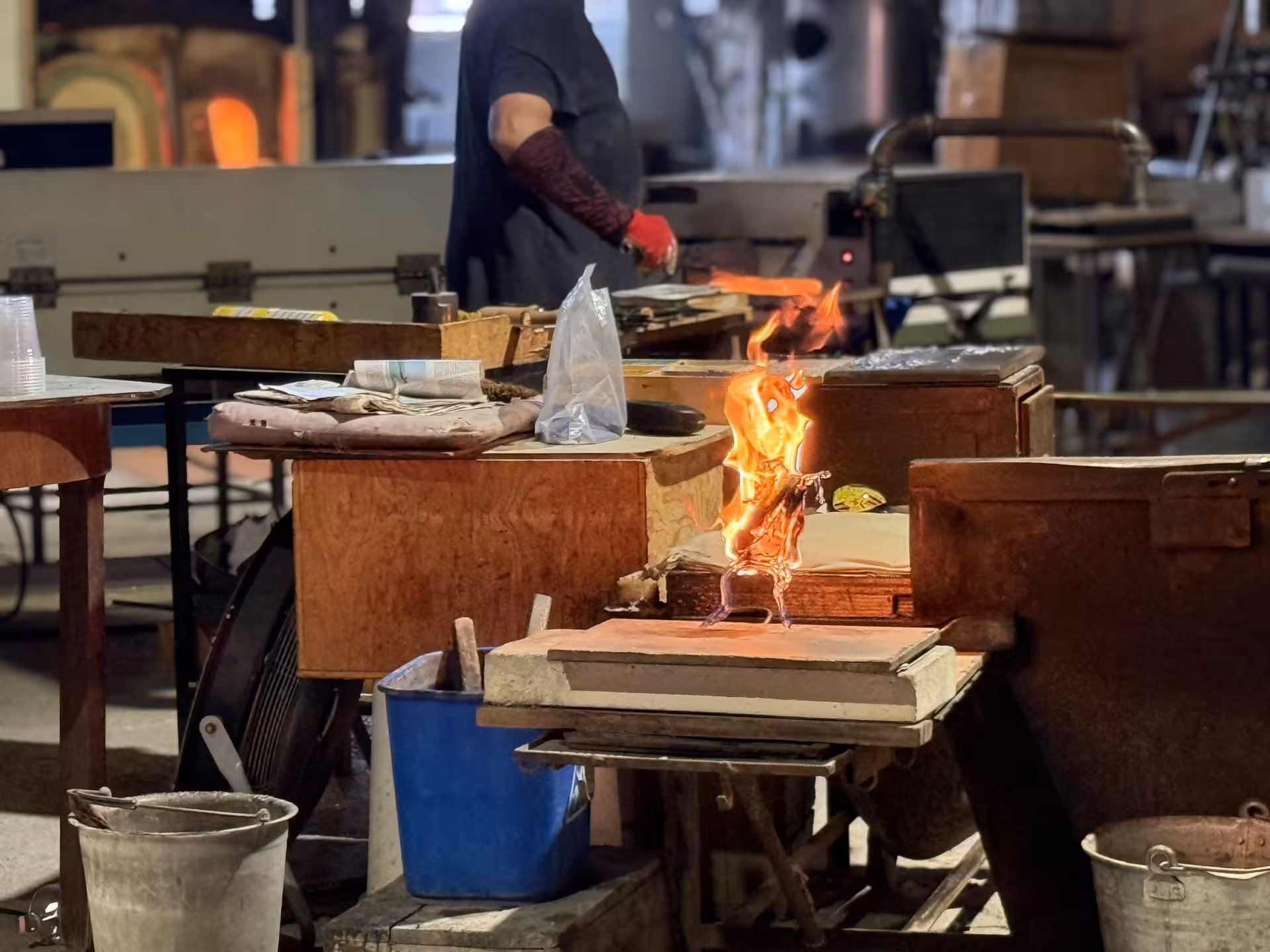 Molten glass being skillfully shaped by a craftsman amid flames in a Murano glass workshop, Venice tour highlight.