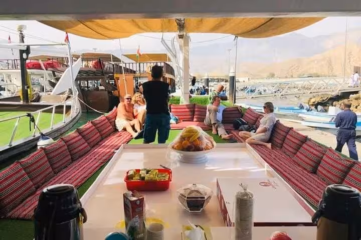 Musandam dhow cruise seating with buffet lunch setup at harbor, ideal for snorkeling and fishing day trip