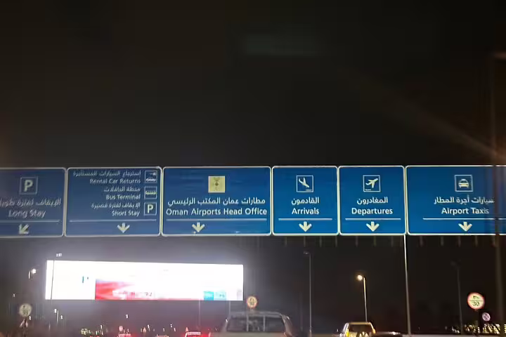 Directional signs at Muscat Airport guiding arrivals, departures, and taxi transfers for seamless travel navigation.