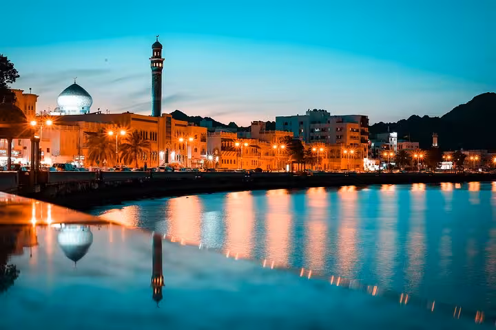 Twilight view of Muttrah Corniche in Muscat with mosque and harbor lights, ideal backdrop for scenic airport transfer rides
