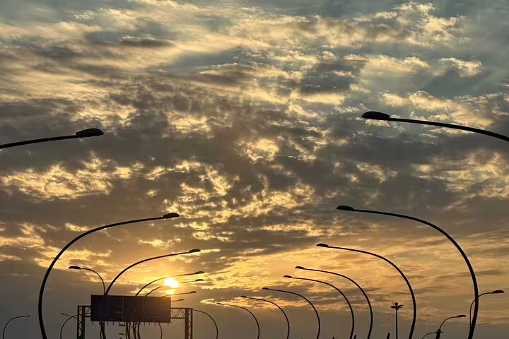 Dramatic sunset with silhouetted streetlights leading to Muscat airport, ideal for taxi transfers and hotel pickups.