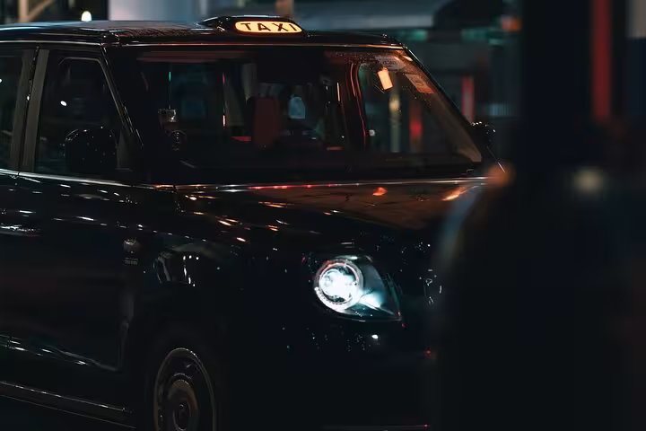Black taxi cab at night with illuminated roof sign, offering reliable Muscat city transfer and hotel pickup