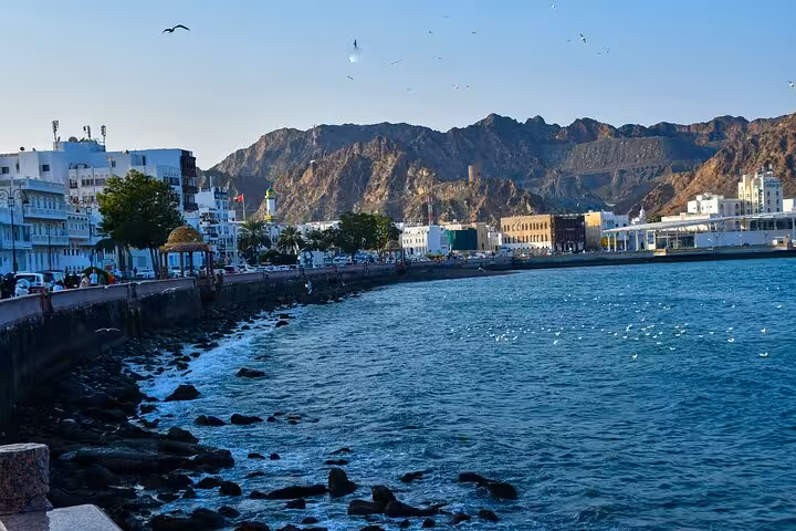 Scenic Muscat Corniche coastline with blue sea, mountains and city promenade, ideal stop on private chauffeur transport tour