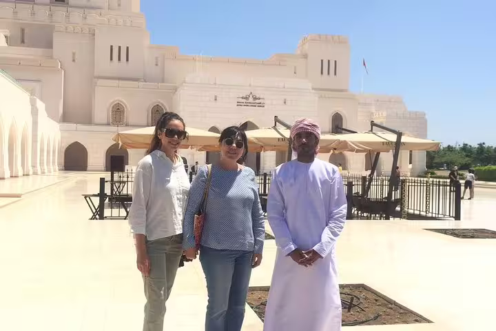 Tourists pose with a local in traditional attire at the Royal Opera House Muscat, highlighting cultural heritage.