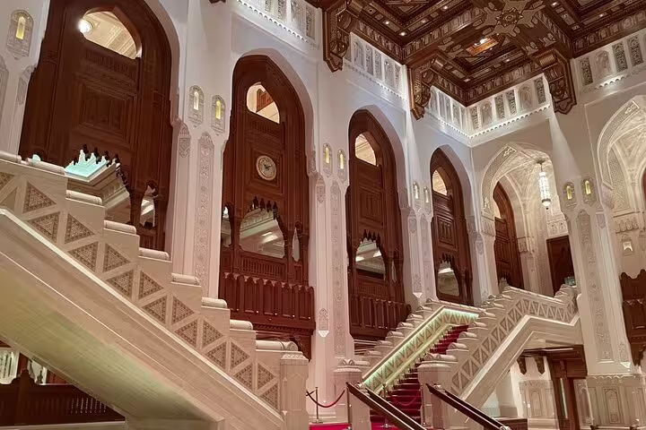 Grand staircase with ornate arches inside a Muscat cultural landmark, showcasing intricate architecture.