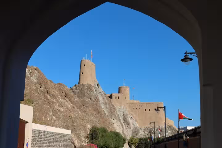 Historic Muscat fort on rocky cliffs framed by an archway, a highlight of private guided tours with transport in Oman