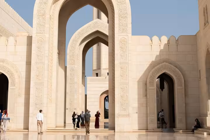Visitors exploring ornate marble archways of Muscat Grand Mosque courtyard, featured on the Half-Day Muscat City Tour