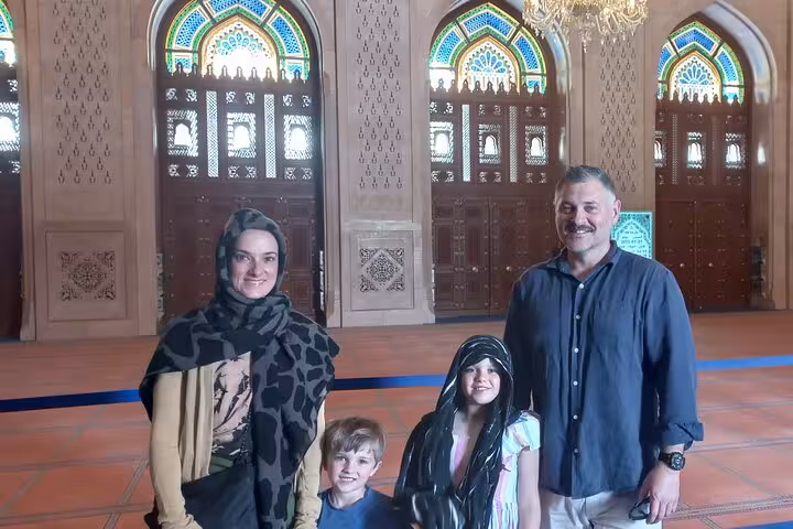 Family inside Muscat’s Grand Mosque, admiring ornate stained-glass windows and chandeliers on an evening taxi sightseeing tour