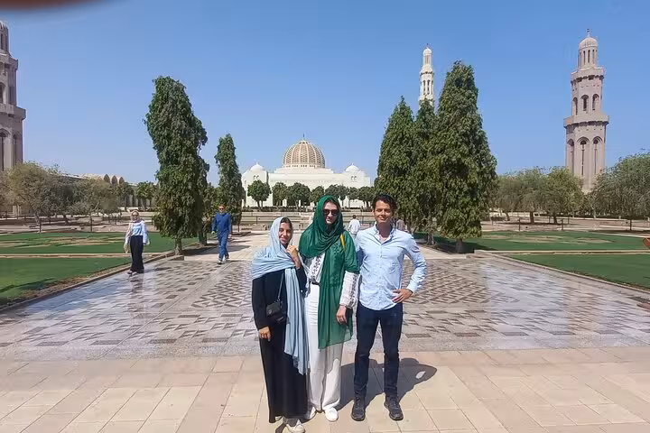 Tourists posing in the landscaped courtyard of Muscat’s Grand Mosque under clear blue skies on an evening taxi sightseeing tour
