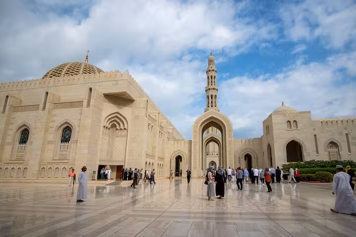 Visitors walking through the polished courtyard of Muscat Grand Mosque with domes and minaret on a private sightseeing tour