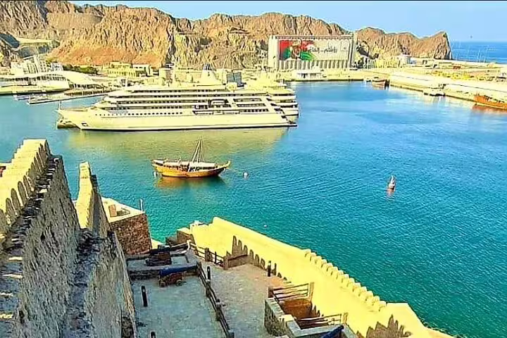Harbor view in Muscat featuring a cruise ship and traditional dhow, highlighting the city's maritime heritage.