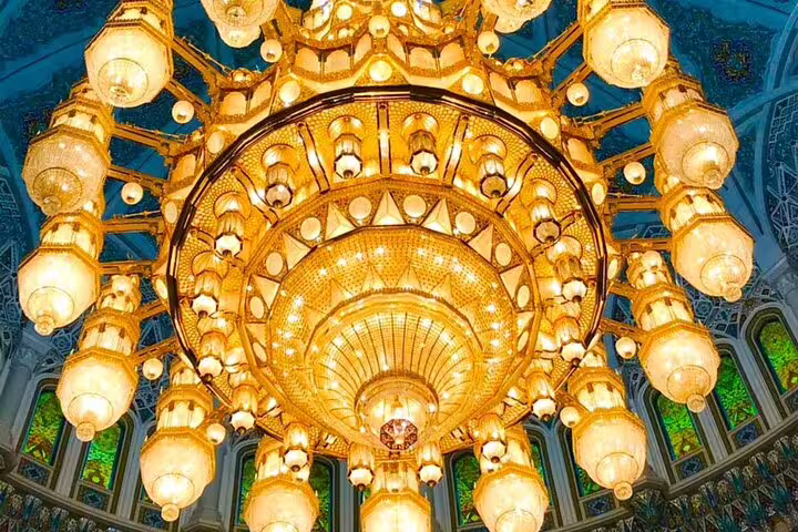 Magnificent chandelier with golden hues and intricate design adorns the ceiling of a Muscat landmark.