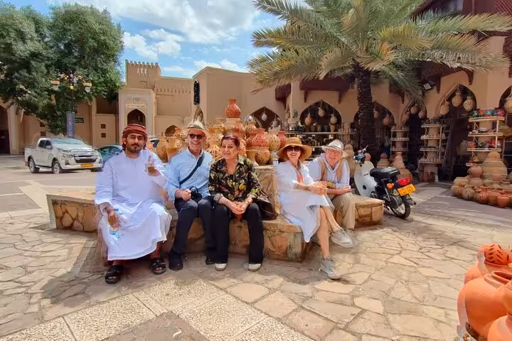 Small group with local guide relaxing in traditional Nizwa souq, surrounded by pottery and palm trees on Muscat day tour