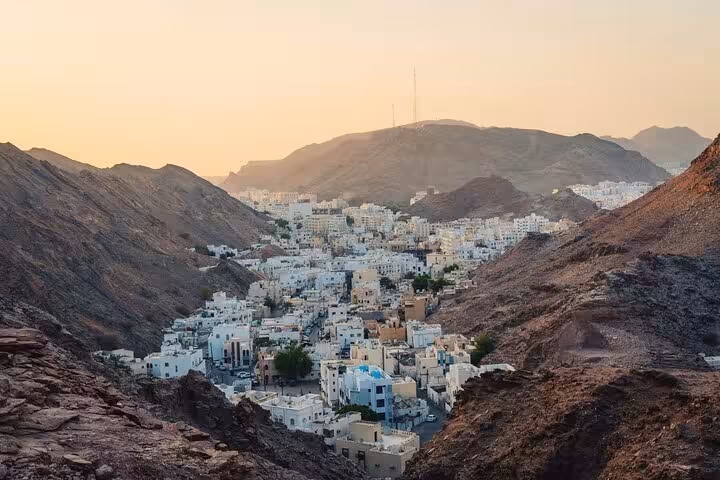 Panoramic view of Muscat old town nestled between rugged mountains at sunset, seen on a private city tour with transport