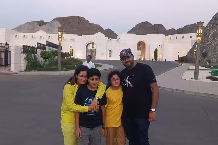Happy family posing outside a grand white palace-style gate during Muscat private city tour with chauffeured transport