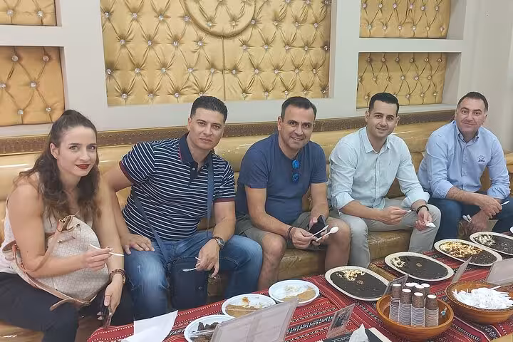 Muscat private tour guests enjoying traditional Omani sweets and coffee in a local majlis with included transport